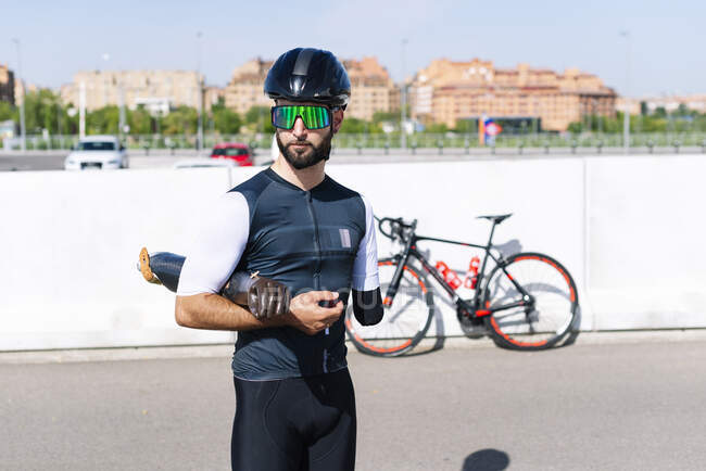 Male amputee athlete holding artificial limb while standing on road during sunny day — Stock Photo