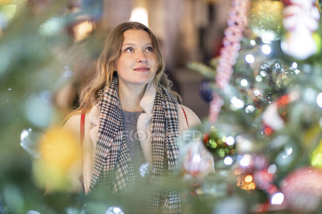 Young woman looking at illuminated Christmas tree and lights in city — Stock Photo