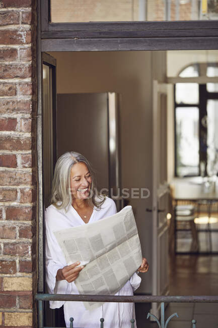 Smiling woman reading newspaper in balcony — Stock Photo