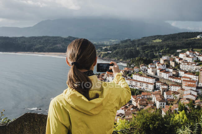 Vista posteriore della donna che fotografa il villaggio attraverso il telefono cellulare durante le vacanze — Foto stock