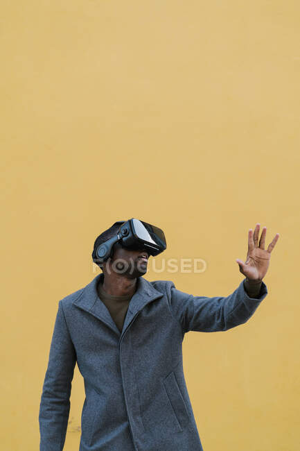 Человек в куртке с помощью гарнитуры виртуальной реальности, стоя напротив желтой стены — стоковое фото