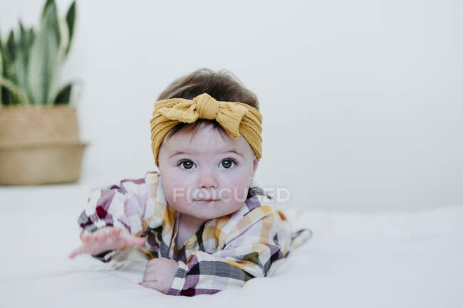 Bambino ragazza indossa arco testa giocare mentre sdraiato sul letto a casa — Foto stock