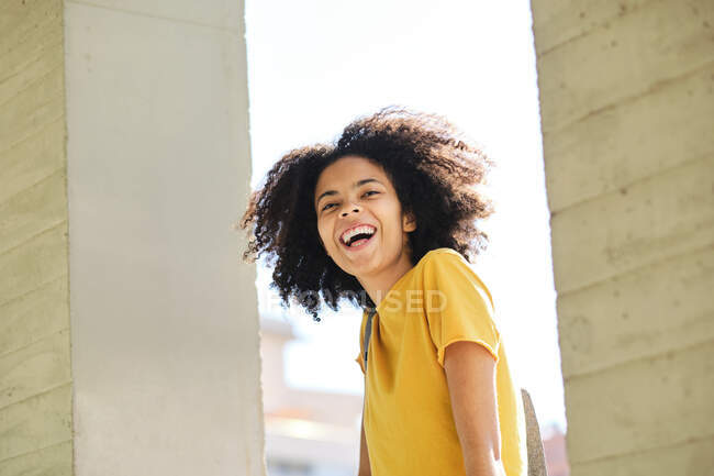 Curly hair student laughing while standing at university - foto de stock