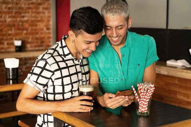 Gay casal partilha móvel telefone em pé na mesa no bar — Fotografia de Stock