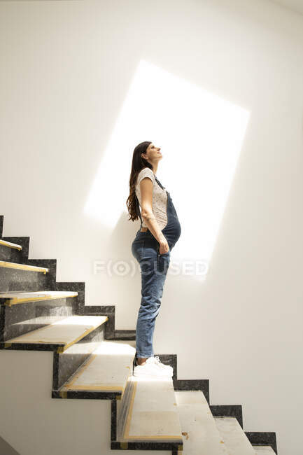 Ragionevole donna incinta guardando in alto mentre in piedi su gradini in una nuova casa — Foto stock