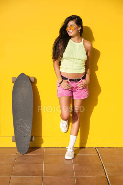 Young beautiful woman posing with longboard in front of yellow wall — Foto stock