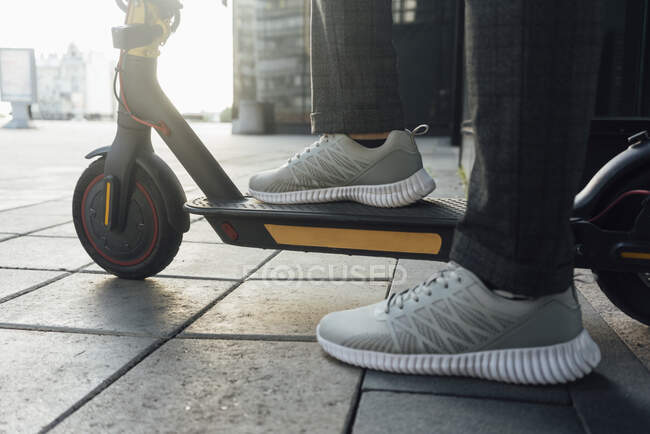Низька секція чоловічого підприємця в спортивному взутті під час їзди на електричному самокаті в центрі міста — стокове фото