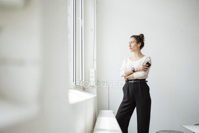 Nachdenkliche Geschäftsfrau mit Smartphone schaut durchs Fenster — Stockfoto