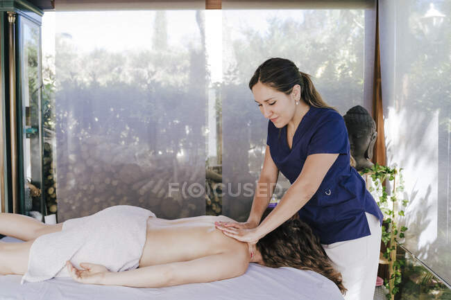Smiling terapeuta mujer dando masaje de espalda a la mujer acostada en la mesa en el spa - foto de stock