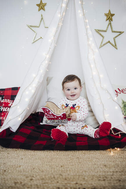 Lächelndes kleines Mädchen spielt mit Kinderwagen-Spielzeug, während es zu Weihnachten zu Hause im Zelt sitzt — Stockfoto
