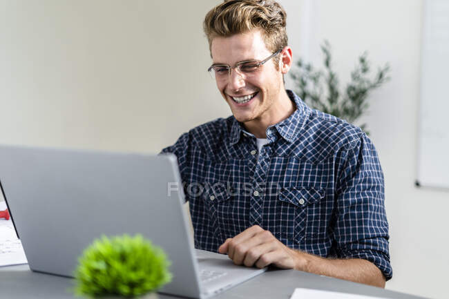 Uomo sorridente utilizzando il computer portatile mentre seduto in ufficio — Foto stock
