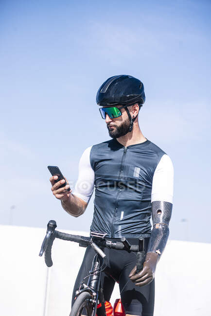 Cycliste amputé masculin utilisant un téléphone intelligent tout en se tenant debout avec le vélo contre le ciel clair — Photo de stock