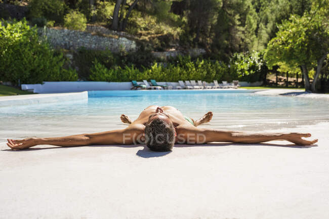 Uomo senza maglietta sdraiato a bordo piscina rilassante nella giornata di sole — Foto stock