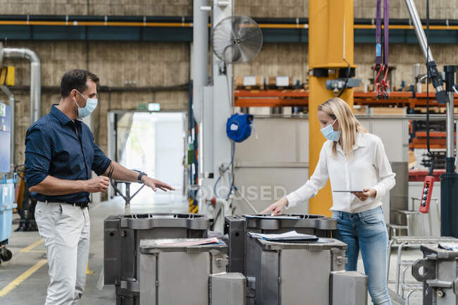 Female entrepreneur and male colleague analyzing machinery while standing in factory during pandemic — Stock Photo