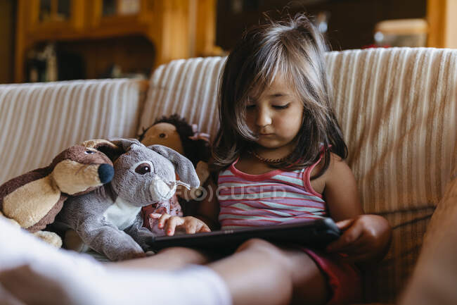Дівчина використовує цифровий планшет, сидячи на дивані вдома — стокове фото