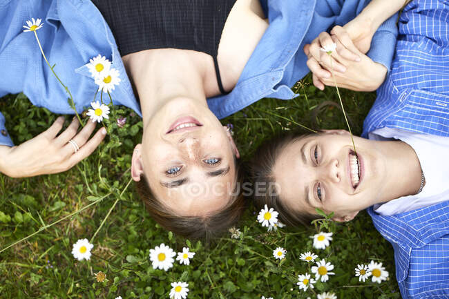 Крупным планом улыбающихся молодых друзей, лежащих на травянистой земле в саду — стоковое фото