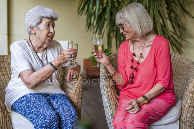 Старшие подруги пьют шампанское, сидя на стульях во внутреннем дворике — стоковое фото