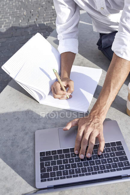 Businessman writing while using laptop in city — Photo de stock
