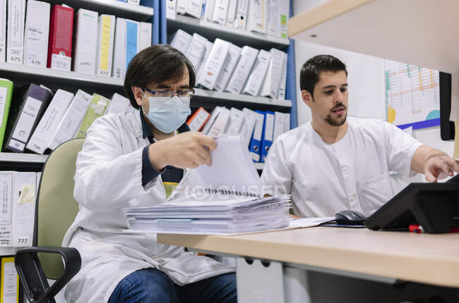 Médicos varones haciendo papeleo en el escritorio en farmacia en el hospital - foto de stock
