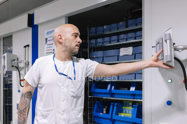 Farmacéutico calvo usando computadora mientras está de pie en la sala de almacenamiento en el hospital - foto de stock