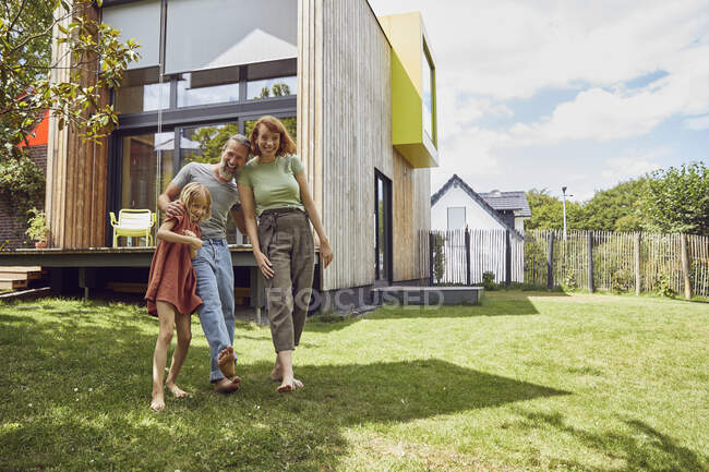 Fröhliche Eltern mit Tochter stehen vor winzigem Haus im Hof — Stockfoto