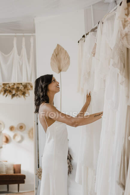 Молода наречена захоплюється одягом, стоячи у весільній майстерні. — стокове фото