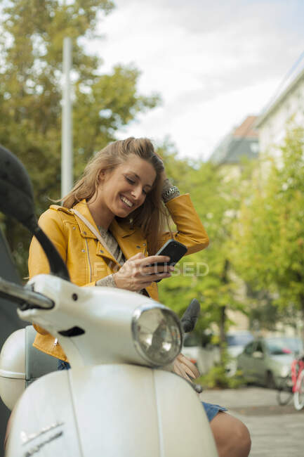 Sorrindo mulher verificando telefone inteligente enquanto sentado em moto — Fotografia de Stock
