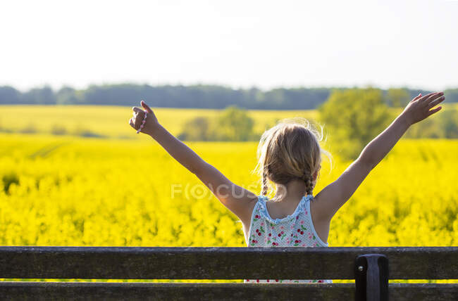 Ragazza con le braccia sollevate seduta nel campo di colza — Foto stock