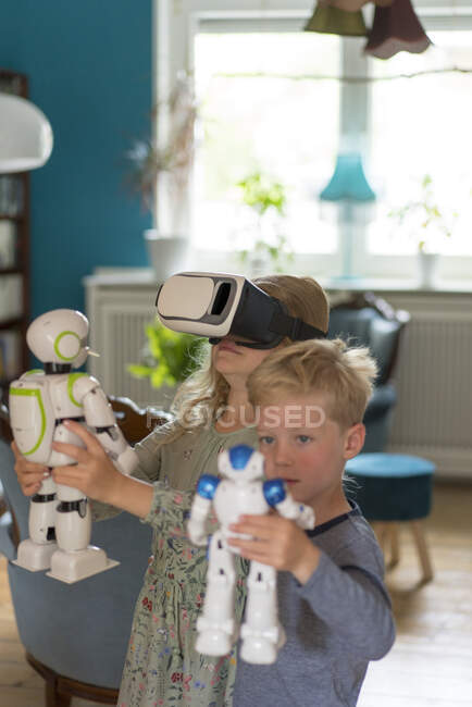 Симпатичные братья и сестры играют с игрушечными роботами и симулятором виртуальной реальности в гостиной дома — стоковое фото