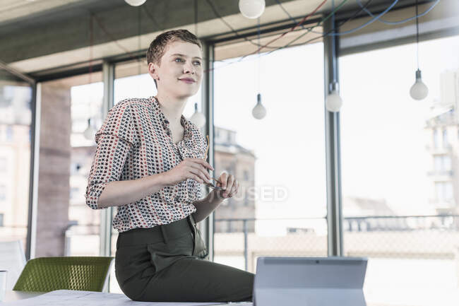 Selbstbewusste Geschäftsfrau sitzt auf Schreibtisch im Büro — Stockfoto