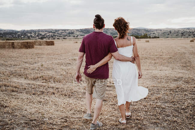 Coppia con braccio intorno a camminare in campo durante il tramonto — Foto stock