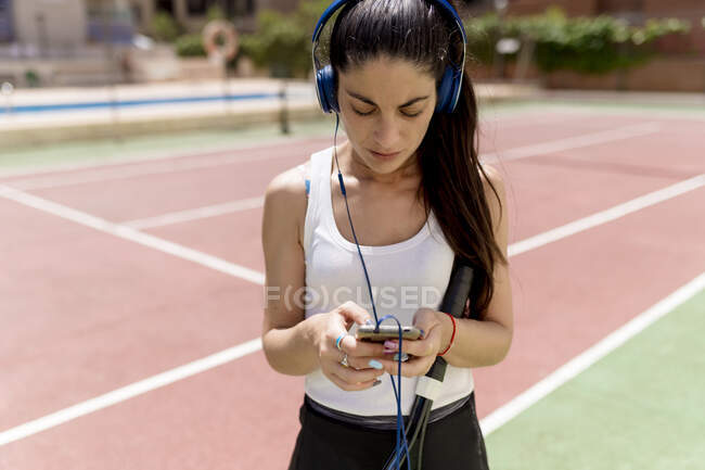Giocatrice di tennis femminile che utilizza lo smartphone mentre ascolta musica in tribunale nella giornata di sole — Foto stock