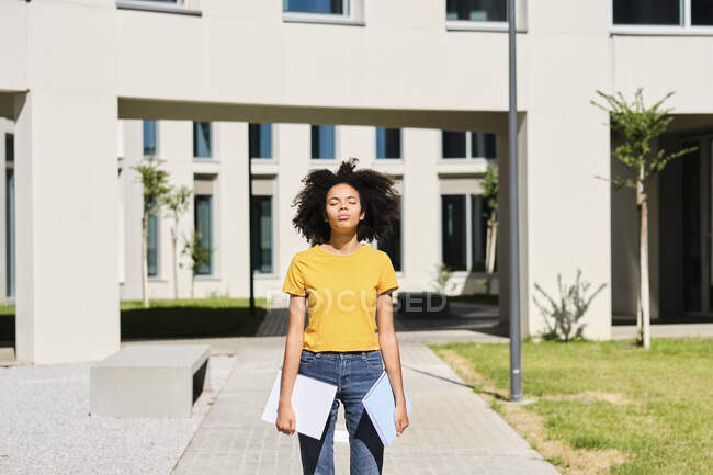 University student holding books while standing with eyes closed at university — Stock Photo