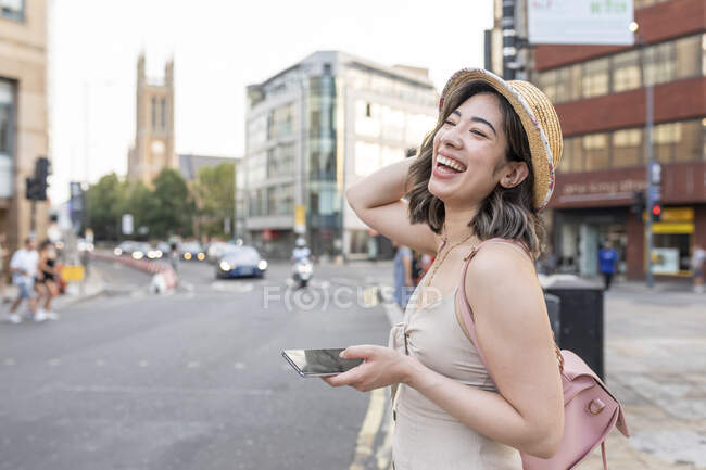 Woman laughing while using smart phone standing on street in city - foto de stock