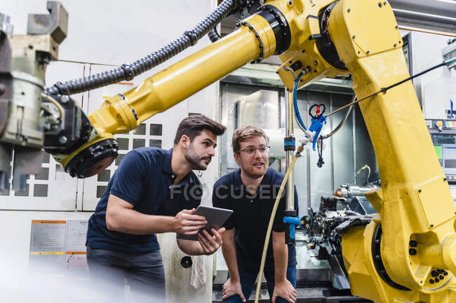 Male coworkers discussing about robotic arm in factory — Stock Photo