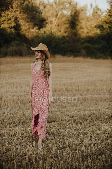 Женщина в платье смотрит в сторону во время прогулки по пшеничному полю на закате — стоковое фото