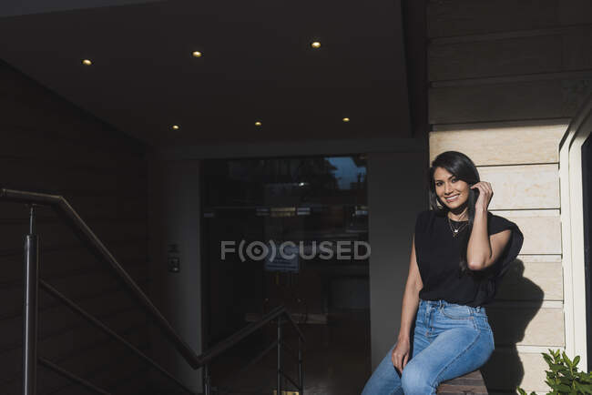 Mujer sonriente sentada fuera del edificio - foto de stock