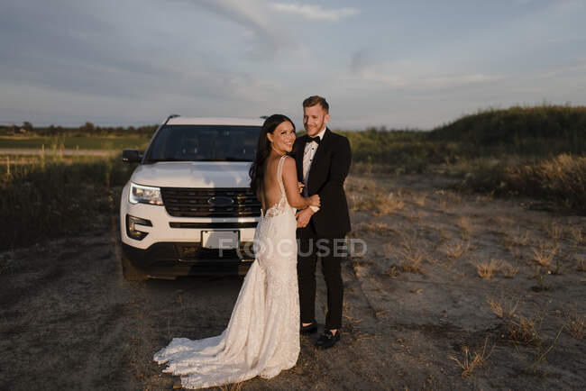 Smiling woman with male partner standing against car in field — Stock Photo