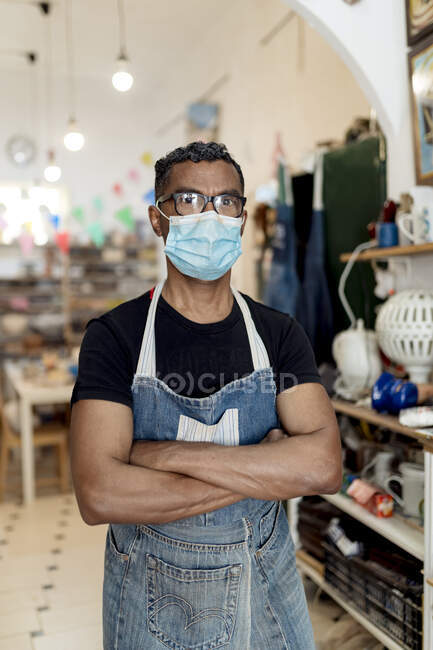 Potier masculin portant un masque avec les bras croisés debout dans l'atelier — Photo de stock