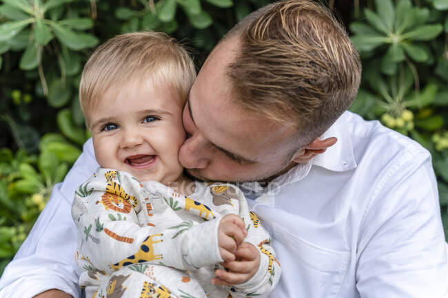 Father kissing baby boy while standing at park — Stock Photo