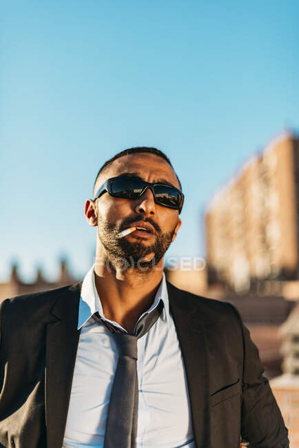 Selbstbewusster männlicher Profi mit Sonnenbrille beim Rauchen auf dem Dach bei klarem Himmel — Stockfoto