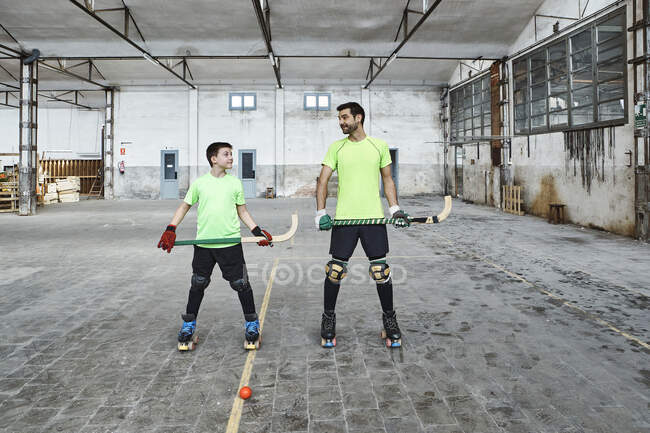Mature man and his son holding hockey sticks while looking at each other — Photo de stock