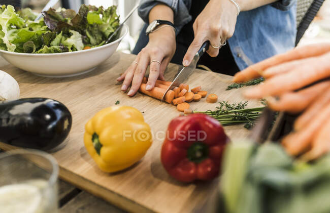 Primer plano de la joven mujer picando zanahorias en la tabla de cortar - foto de stock