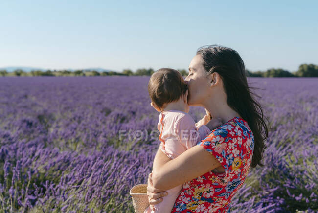Femme debout dans un vaste champ de lavande avec bébé fille dans les mains — Photo de stock