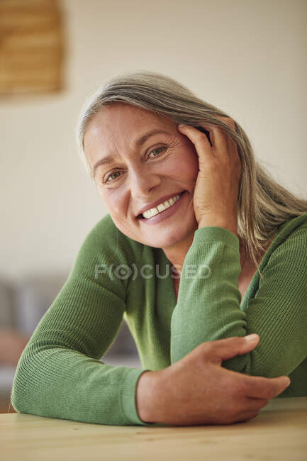 Mulher feliz com a mão na bochecha sentada à mesa em casa — Fotografia de Stock