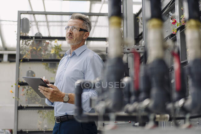 Professionista di sesso maschile con tablet digitale esaminando apparecchiature di irrigazione in vivaio — Foto stock