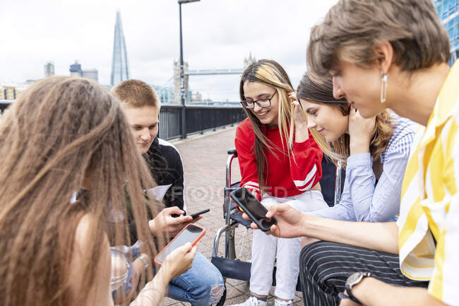 Amis masculins et féminins utilisant des téléphones mobiles tout en passant du temps libre ensemble en ville — Photo de stock