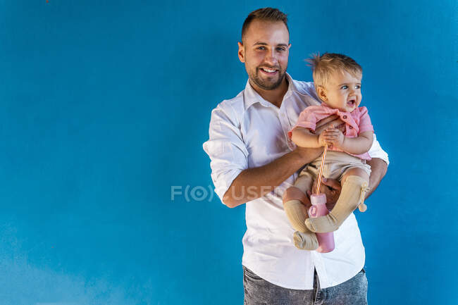 Padre sorridente che porta il bambino mentre sta in piedi contro il muro blu — Foto stock
