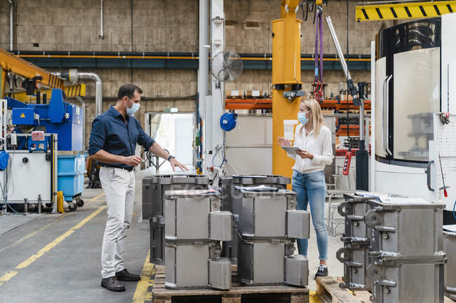 Homme d'affaires examinant des machines avec une collègue féminine dans l'industrie pendant la COVID-19 — Photo de stock