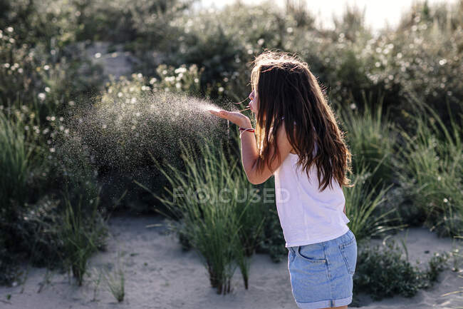 Ragazza che soffia mentre in piedi sulla sabbia durante la giornata di sole — Foto stock